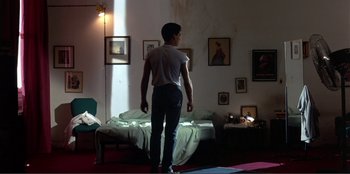 Movie still from “Law of Desire” (1987), directed by Pedro Almodóvar – A man standing in front of a bed in a room; Wide shot, Low angle