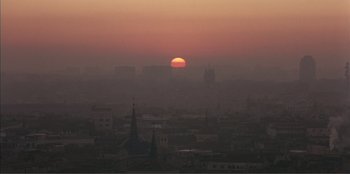 Movie still from “Law of Desire” (1987), directed by Pedro Almodóvar – The sun is setting over a city skyline; Extreme Wide shot, High angle