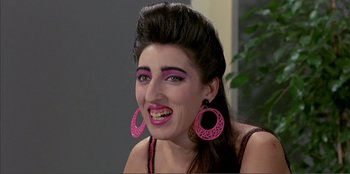 Movie still from “Law of Desire” (1987), directed by Pedro Almodóvar – A woman with pink lipstick and pink earrings is smiling; Close Up shot, High angle
