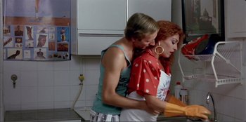 Movie still from “Law of Desire” (1987), directed by Pedro Almodóvar – Two women are hugging in the kitchen together; Medium shot, Over the shoulder angle