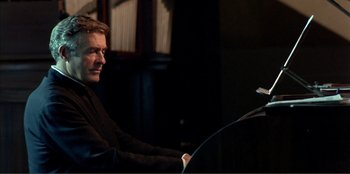 Movie still from “Law of Desire” (1987), directed by Pedro Almodóvar – A man sitting in front of a microphone in a dark room; Close Up shot, Low angle