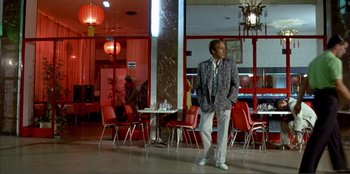 Movie still from “Law of Desire” (1987), directed by Pedro Almodóvar – A man in a suit and tie standing in front of red chairs; Wide shot, Low angle