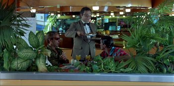 Movie still from “Law of Desire” (1987), directed by Pedro Almodóvar – Three people sitting at a table with a plate of food; Medium shot, Over the shoulder angle