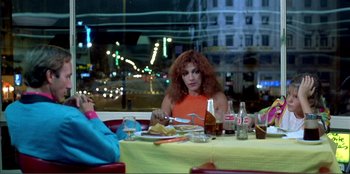 Movie still from “Law of Desire” (1987), directed by Pedro Almodóvar – A woman sitting at a table with a plate of food; Medium shot, Low angle