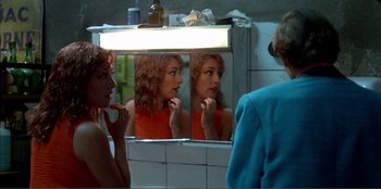 Movie still from “Law of Desire” (1987), directed by Pedro Almodóvar – A woman looking in the mirror brushing her teeth; Medium shot, Over the shoulder angle