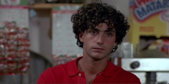 Movie still from “Law of Desire” (1987), directed by Pedro Almodóvar – A young man with curly black hair wearing a red shirt looking at the camera; Close Up shot, Over the shoulder angle