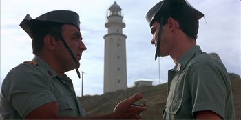 Movie still from “Law of Desire” (1987), directed by Pedro Almodóvar – Two men talking in front of a light house; Medium shot, Low angle