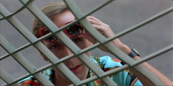 Movie still from “Law of Desire” (1987), directed by Pedro Almodóvar – A person with sunglasses looking through a metal fence; Close Up shot, Overhead angle