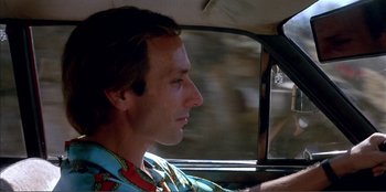 Movie still from “Law of Desire” (1987), directed by Pedro Almodóvar – A man sitting in the driver's seat of a car; Close Up shot, Low angle