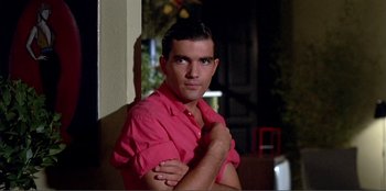 Movie still from “Law of Desire” (1987), directed by Pedro Almodóvar – A man in a red shirt is posing for a picture; Close Up shot, Low angle