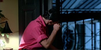Movie still from “Law of Desire” (1987), directed by Pedro Almodóvar – A woman in a pink shirt is sitting on a ledge; Medium shot, High angle