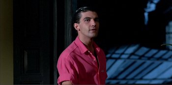 Movie still from “Law of Desire” (1987), directed by Pedro Almodóvar – A man in a pink shirt is looking at the camera; Close Up shot, Low angle