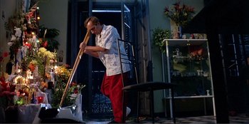 Movie still from “Law of Desire” (1987), directed by Pedro Almodóvar – A man in white shirt and red pants holding a broom; Wide shot, Low angle