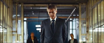 Movie still from “Layer Cake” (2004), directed by Matthew Vaughn – A man in a suit and tie standing in front of two other men; Medium shot, Low angle