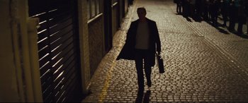 Movie still from “Layer Cake” (2004), directed by Matthew Vaughn – A woman walking down a brick street holding a briefcase; Wide shot, Low angle