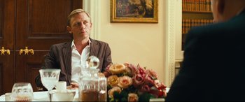 Movie still from “Layer Cake” (2004), directed by Matthew Vaughn – A man sitting in front of a vase of flowers; Medium shot, Over the shoulder angle