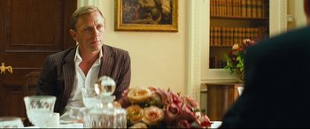 Movie still from “Layer Cake” (2004), directed by Matthew Vaughn – A man sitting at a table with a vase of flowers; Medium shot, Over the shoulder angle
