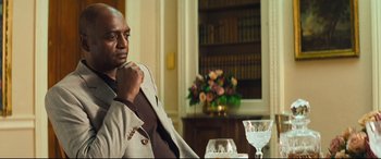 Movie still from “Layer Cake” (2004), directed by Matthew Vaughn – A man sitting at a table with a glass of wine; Medium shot, Low angle