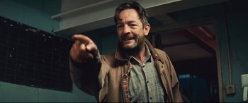 Movie still from “Layer Cake” (2004), directed by Matthew Vaughn – A man in a plaid shirt and a brown jacket holding a pen; Close Up shot, Over the shoulder angle