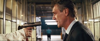 Movie still from “Layer Cake” (2004), directed by Matthew Vaughn – A man in a suit and tie holding a gun in his hand; Close Up shot, Over the shoulder angle