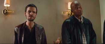 Movie still from “Layer Cake” (2004), directed by Matthew Vaughn – Two men standing next to each other in front of a wall; Close Up shot, Over the shoulder angle