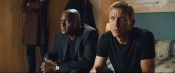 Movie still from “Layer Cake” (2004), directed by Matthew Vaughn – A couple of men sitting next to each other on the ground; Close Up shot, Over the shoulder angle