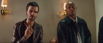 Movie still from “Layer Cake” (2004), directed by Matthew Vaughn – Two men are standing next to each other in a room; Close Up shot, Over the shoulder angle