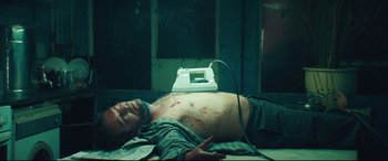Movie still from “Layer Cake” (2004), directed by Matthew Vaughn – A man laying on the ground with blood on his chest; Medium shot, Overhead angle