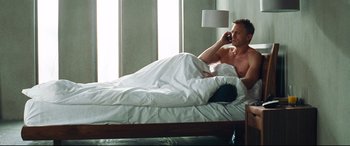 Movie still from “Layer Cake” (2004), directed by Matthew Vaughn – A man laying in bed talking on a phone; Medium shot, Overhead angle