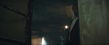 Movie still from “Layer Cake” (2004), directed by Matthew Vaughn – A man standing in a dark room with a microphone; Medium shot, Low angle