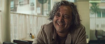 Movie still from “Layer Cake” (2004), directed by Matthew Vaughn – A person with a beard smiling; Close Up shot, Low angle