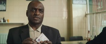 Movie still from “Layer Cake” (2004), directed by Matthew Vaughn – A man in a black suit holding money in his hands; Close Up shot, Low angle