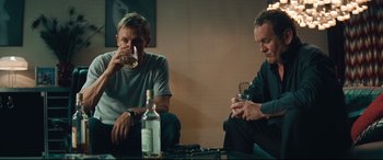 Movie still from “Layer Cake” (2004), directed by Matthew Vaughn – Two men sitting at a table with a glass of wine; Medium shot, Low angle