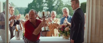 Movie still from “Layer Cake” (2004), directed by Matthew Vaughn – A group of men standing around a table with a trophy; Medium shot, Over the shoulder angle