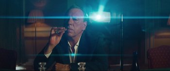 Movie still from “Layer Cake” (2004), directed by Matthew Vaughn – A man sitting at a table with a cigarette in his mouth; Medium shot, Low angle