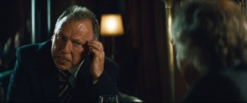 Movie still from “Layer Cake” (2004), directed by Matthew Vaughn – An older man sitting at a table with a glass of red wine; Close Up shot, Over the shoulder angle