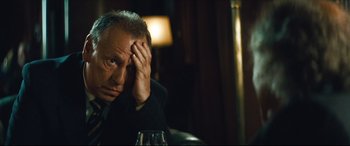Movie still from “Layer Cake” (2004), directed by Matthew Vaughn – A man sitting at a table with his hand on his head; Close Up shot, Low angle