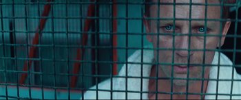 Movie still from “Layer Cake” (2004), directed by Matthew Vaughn – A man with blue eyes behind a metal fence; Close Up shot, Overhead angle