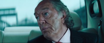 Movie still from “Layer Cake” (2004), directed by Matthew Vaughn – An older man with long green hair and a red tie; Close Up shot, Over the shoulder angle
