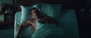 Movie still from “Layer Cake” (2004), directed by Matthew Vaughn – A man laying in a bed under a white blanket; Medium shot, Overhead angle