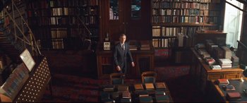 Movie still from “Layer Cake” (2004), directed by Matthew Vaughn – A man in a suit standing in front of a table of books; Wide shot, High angle