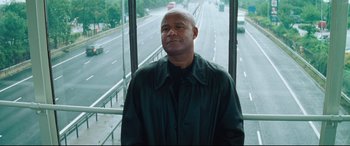 Movie still from “Layer Cake” (2004), directed by Matthew Vaughn – A man standing in front of a window on the side of a road; Medium shot, Low angle