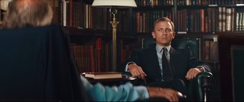 Movie still from “Layer Cake” (2004), directed by Matthew Vaughn – A man in a suit sitting in front of a table; Medium shot, Over the shoulder angle
