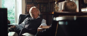 Movie still from “Layer Cake” (2004), directed by Matthew Vaughn – An older man sitting in a chair in a library; Medium shot, Over the shoulder angle