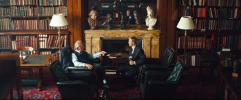Movie still from “Layer Cake” (2004), directed by Matthew Vaughn – Two men sitting in chairs in front of a fire place; Wide shot, Over the shoulder angle