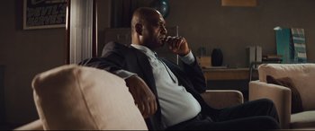 Movie still from “Layer Cake” (2004), directed by Matthew Vaughn – A man sitting on a couch with his hand under his chin; Medium shot, Low angle