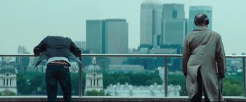 Movie still from “Layer Cake” (2004), directed by Matthew Vaughn – A bird sitting on a railing in front of a city skyline; Wide shot, Over the shoulder angle