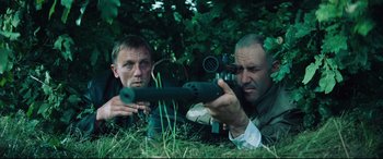 Movie still from “Layer Cake” (2004), directed by Matthew Vaughn – Two men are laying in the grass with a rifle; Medium shot, Low angle
