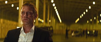 Movie still from “Layer Cake” (2004), directed by Matthew Vaughn – A man in a suit and tie in a dark room; Close Up shot, Over the shoulder angle