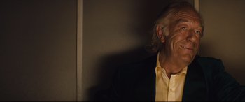 Movie still from “Layer Cake” (2004), directed by Matthew Vaughn – An older man wearing a yellow button down shirt; Close Up shot, Low angle